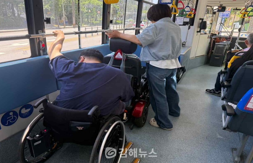 장애인 탑승이 가능한 저상버스이지만 휠체어 고정장치가 없어 손으로 손잡이를 잡고 있는 한 장애인의 모습. / 김해장애인인권센터